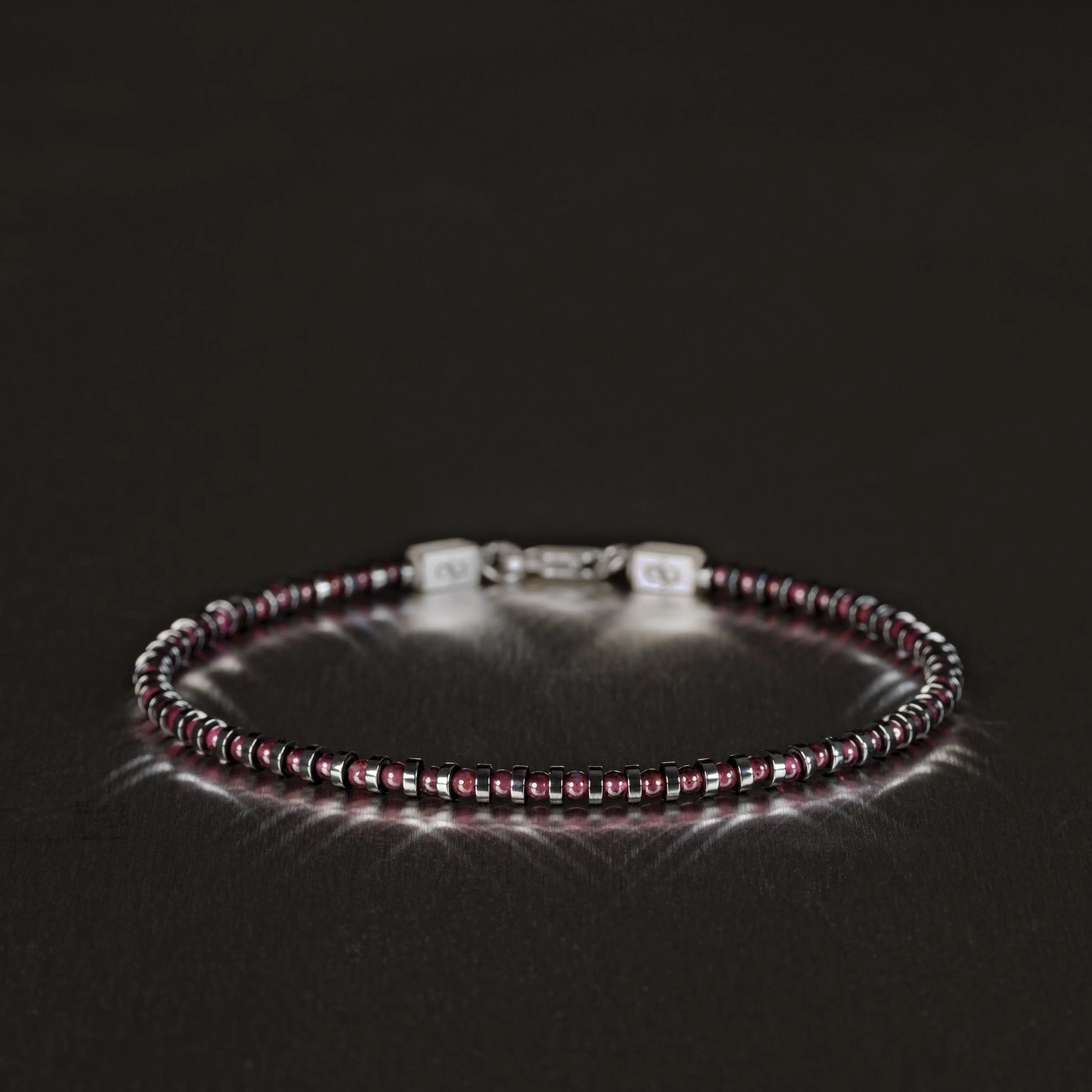 Red Garnet Bracelet XIII with 2mm stones and silver lock, featuring hematite accents, displayed on a dark reflective surface.